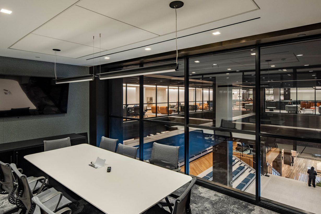 A WorkLife Office Suites by Industrious conference room with a glass window wall peering out into the building common areas and staircase.