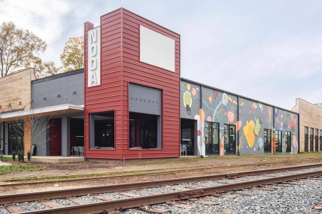 The exterior of Industrious' Charlotte NoDa location, a building with a red and grey exterior and a colorful mural decorating its side. The structure was formerly a warehouse but was repurposed for flex work through adaptive reuse projects.
