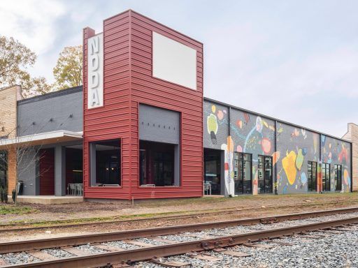 The exterior of Industrious' Charlotte NoDa location, a building with a red and grey exterior and a colorful mural decorating its side. The structure was formerly a warehouse but was repurposed for flex work through adaptive reuse projects.